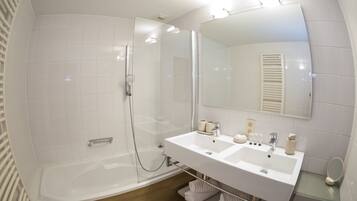 Un baño moderno con ducha de vidrio, lavamanos blanco doble y un espejo grande.