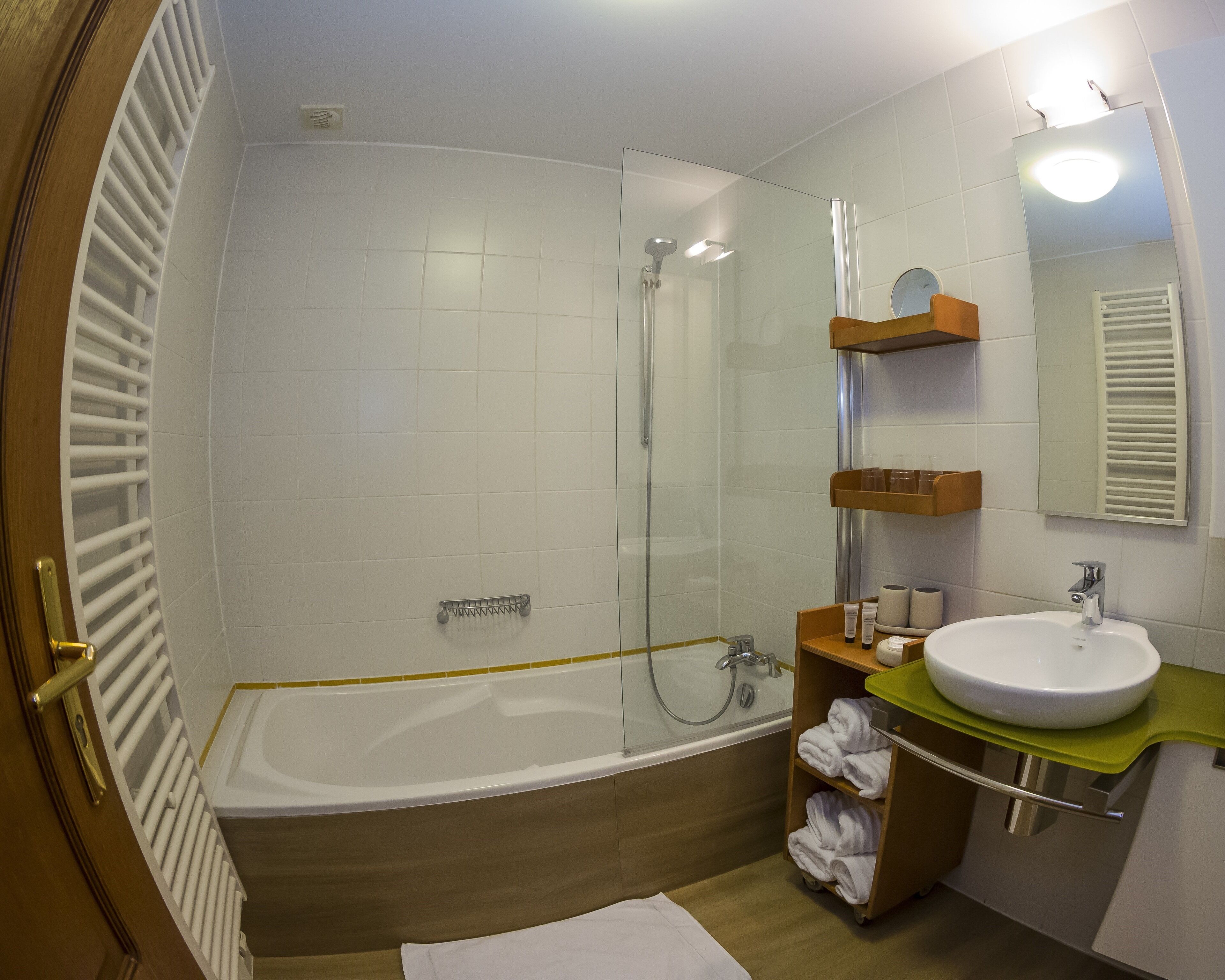 A modern bathroom with a glass-enclosed shower, a bathtub, a sink with a green countertop, and a mirror with a light above it.