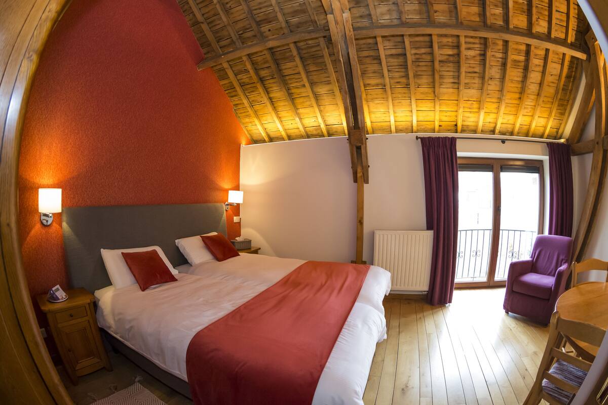 Un dormitorio con una cama grande, techo de madera y un balcón con cortinas moradas.