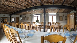 Un comedor con una larga mesa dispuesta para una comida, sillas de madera y techo de ladrillo.