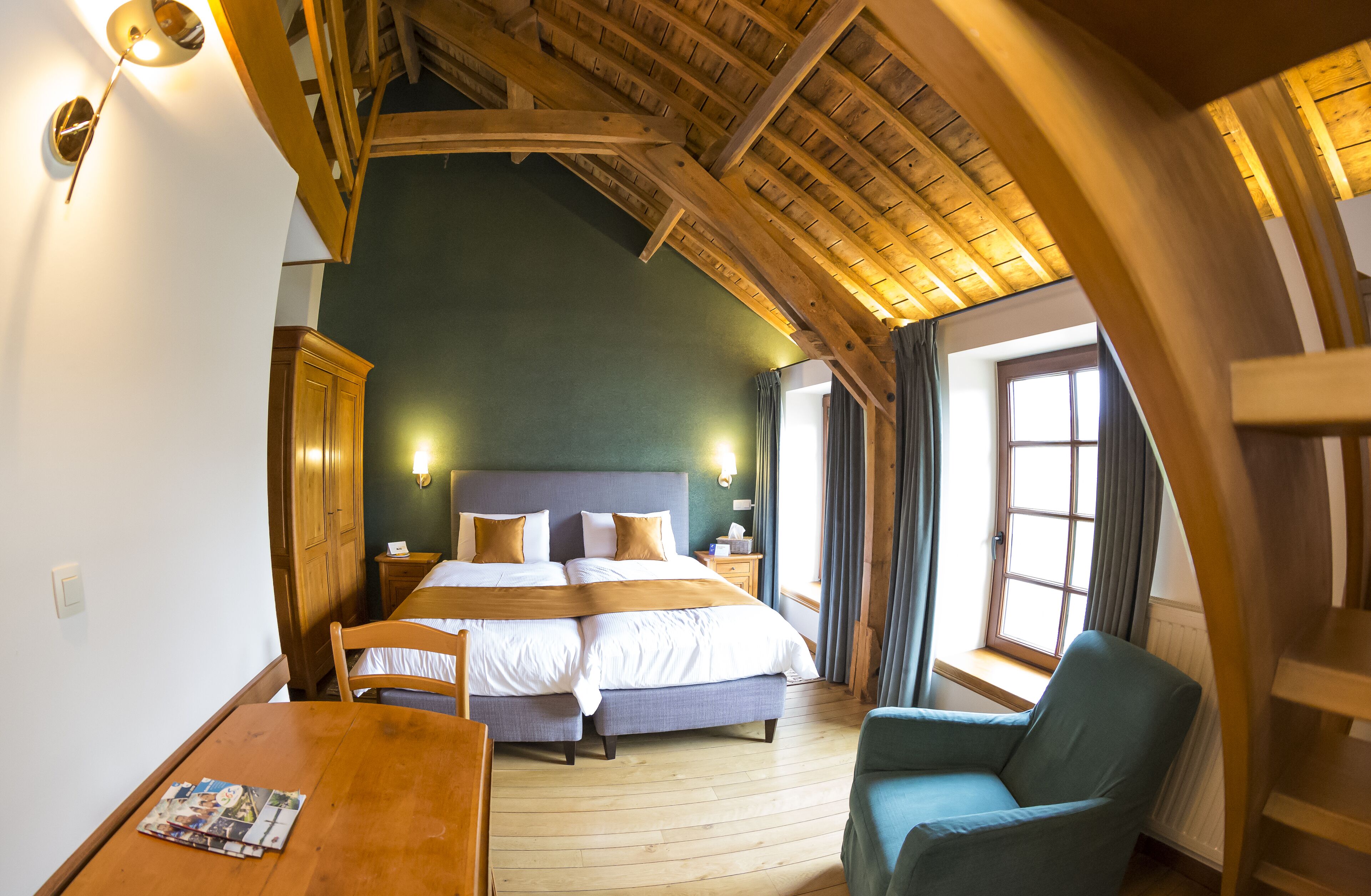 A bedroom with a large bed, wooden ceiling beams, a nightstand, a chair, and a table with a magazine.