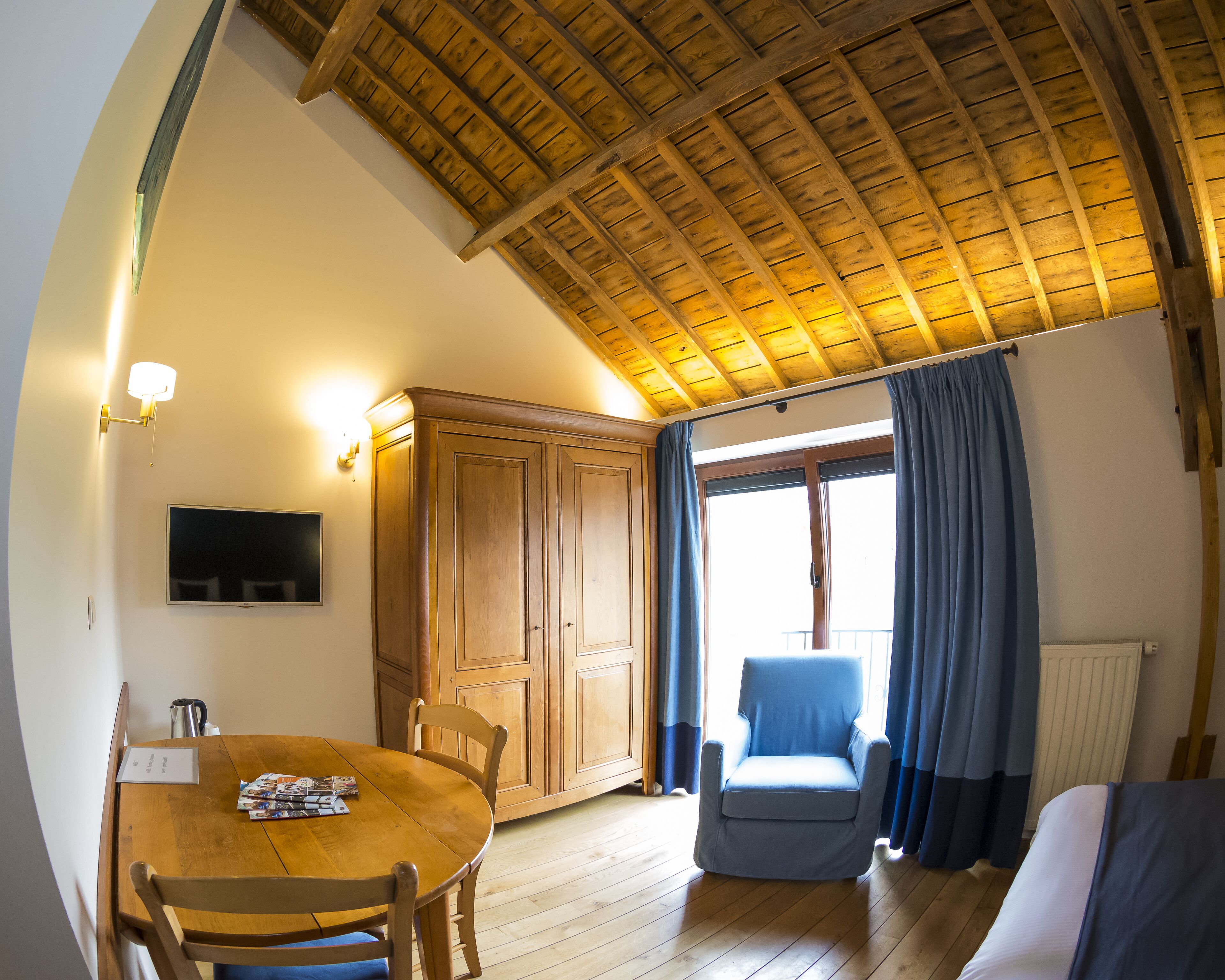Une pièce avec un plafond en bois, une table à manger avec des chaises, un téléviseur, une armoire, une fenêtre avec des rideaux et un canapé.