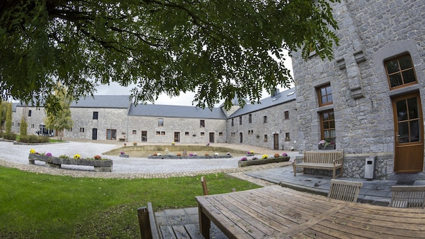 Un patio con un edificio de piedra, bancos de madera y parterres de flores.