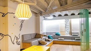 A modern living room with a sectional sofa, a yellow table, and a large window with a view. - River Hostel (Valencia)