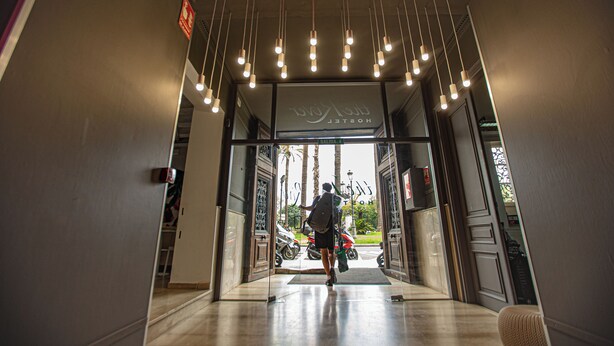 A hotel entrance with a motorbike parked outside, a sign above the doors, and hanging lights. - River Hostel (Valencia)