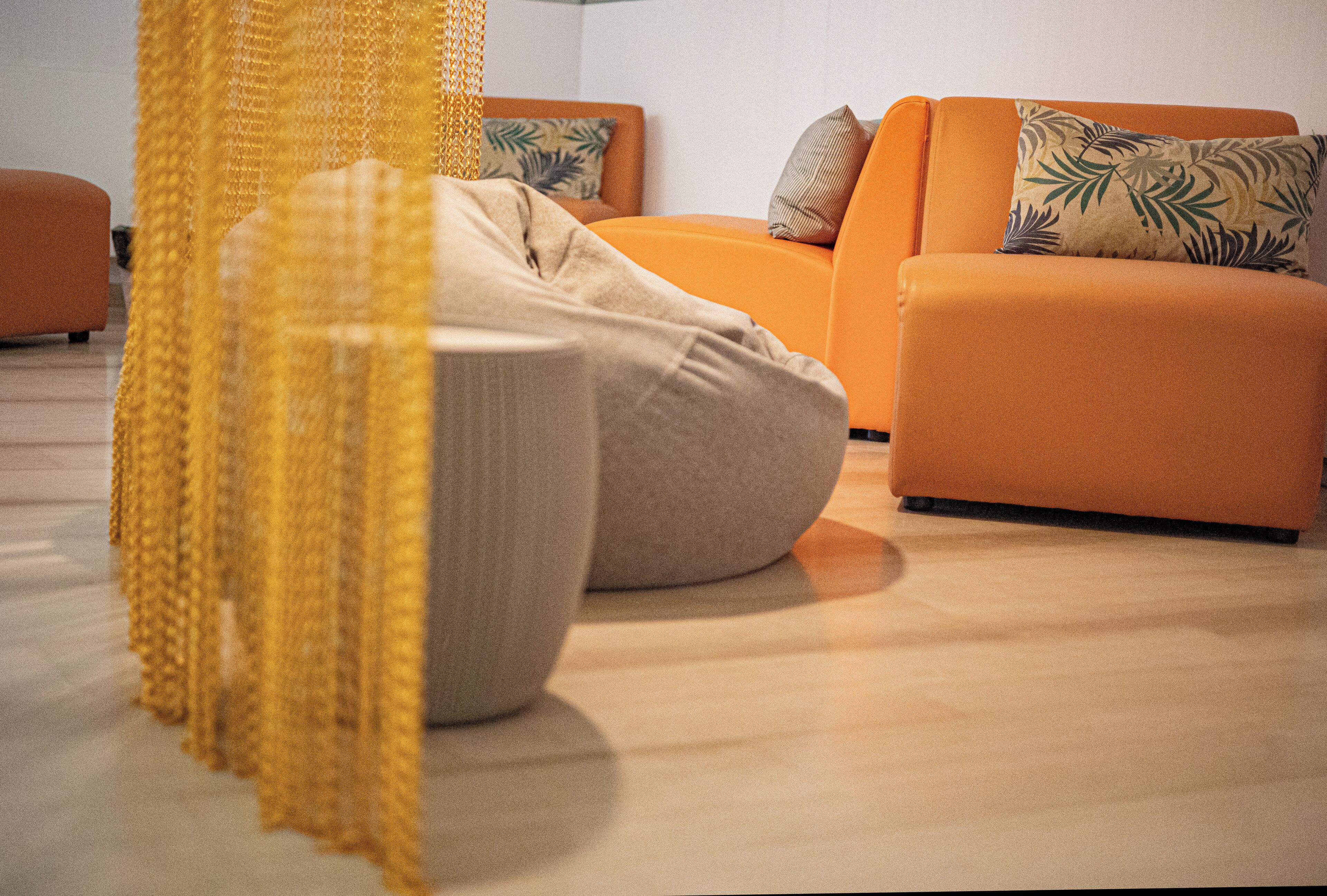A modern living room with a sofa and a bean bag chair, a yellow curtain, and a patterned pillow.