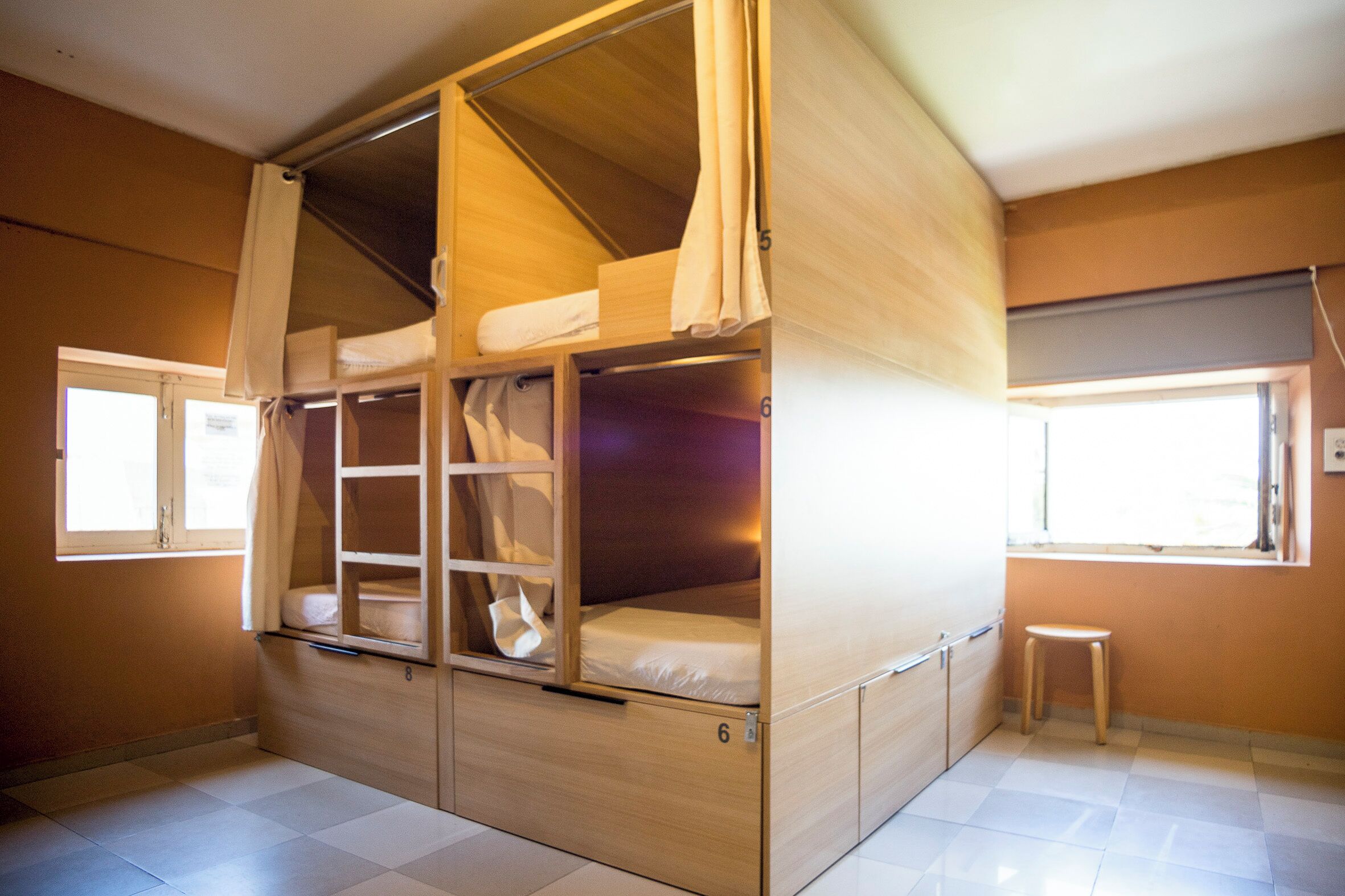 Una habitación con literas, un taburete pequeño y una ventana.