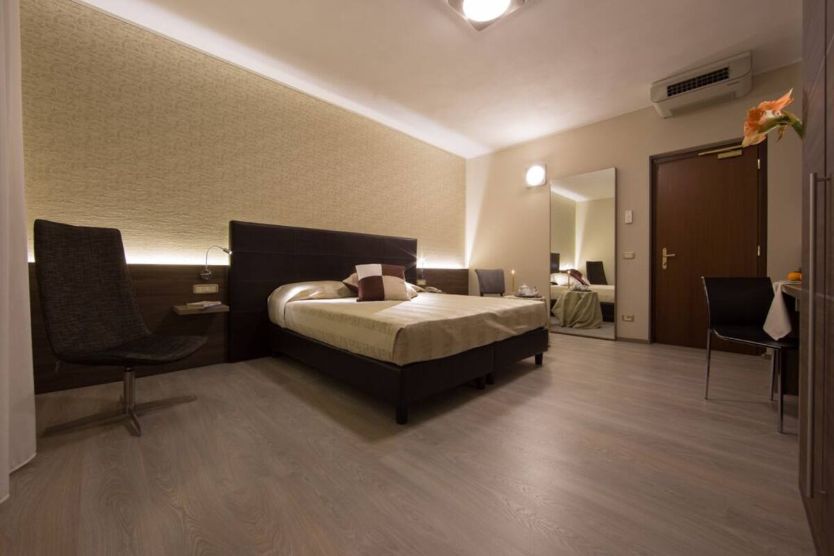 Une chambre d’hôtel moderne avec un grand lit, un coin salon comprenant un fauteuil, une petite table et un miroir.