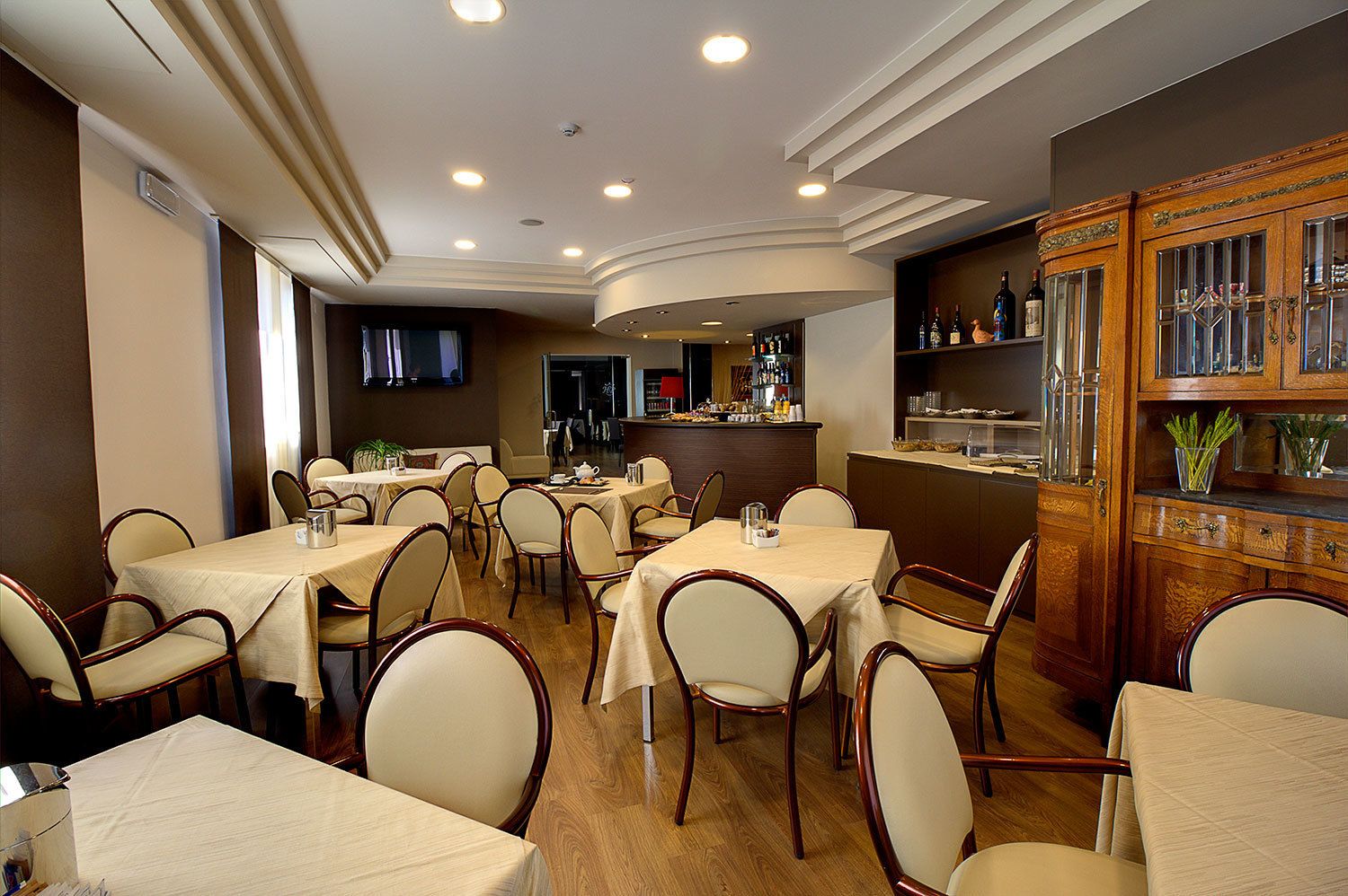 Un restaurant avec plusieurs tables et chaises, un bar avec des bouteilles exposées et un écran de télévision fixé au mur.