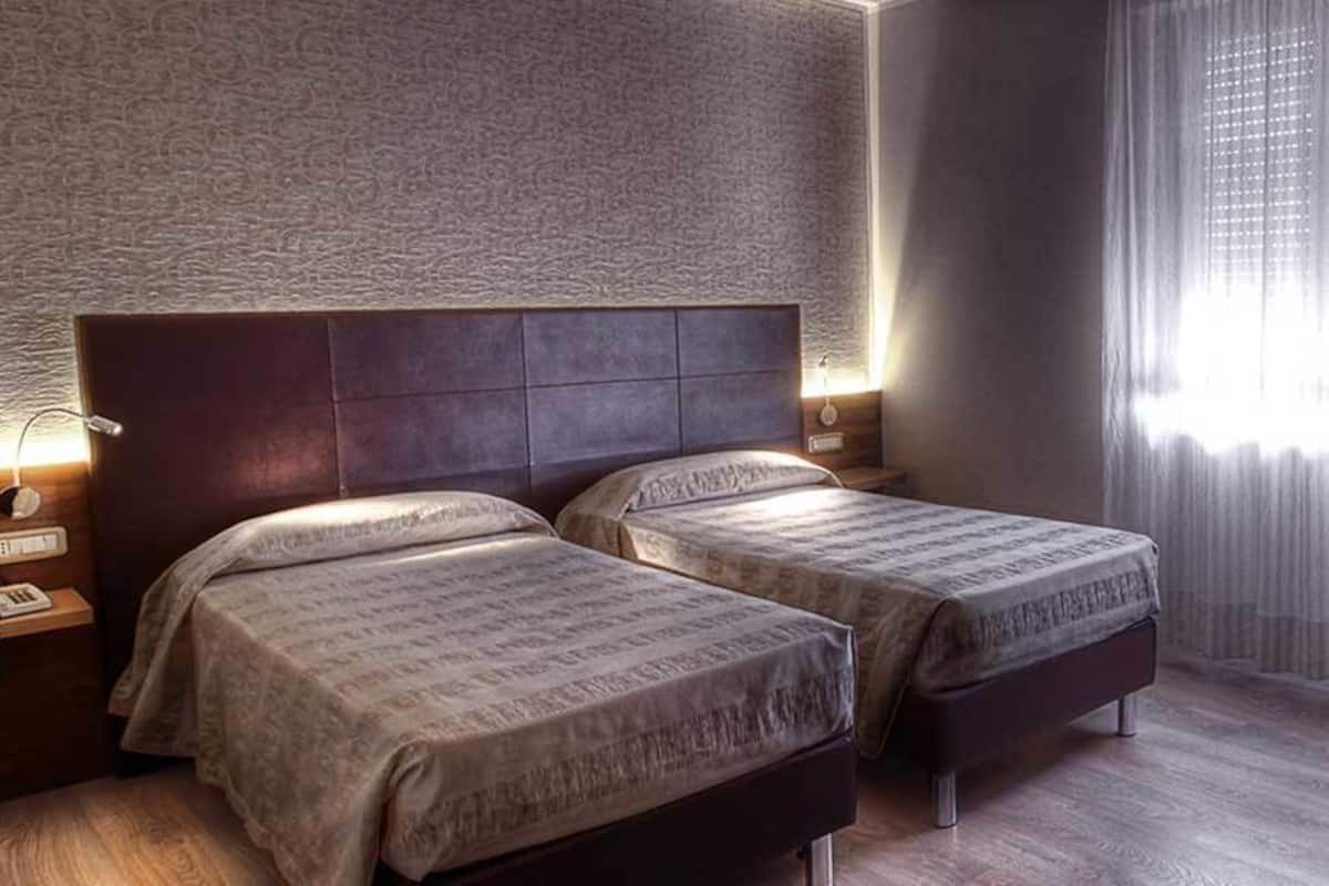 Une chambre d’hôtel avec deux lits, un bureau avec une chaise, un téléphone et une fenêtre avec des rideaux.