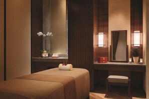 A hotel room with a bed, a small bench, a vanity with a mirror, and a potted plant.