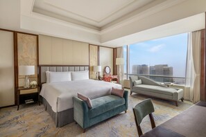 A hotel room with a large bed, a sofa, a chair, and a view of the city.