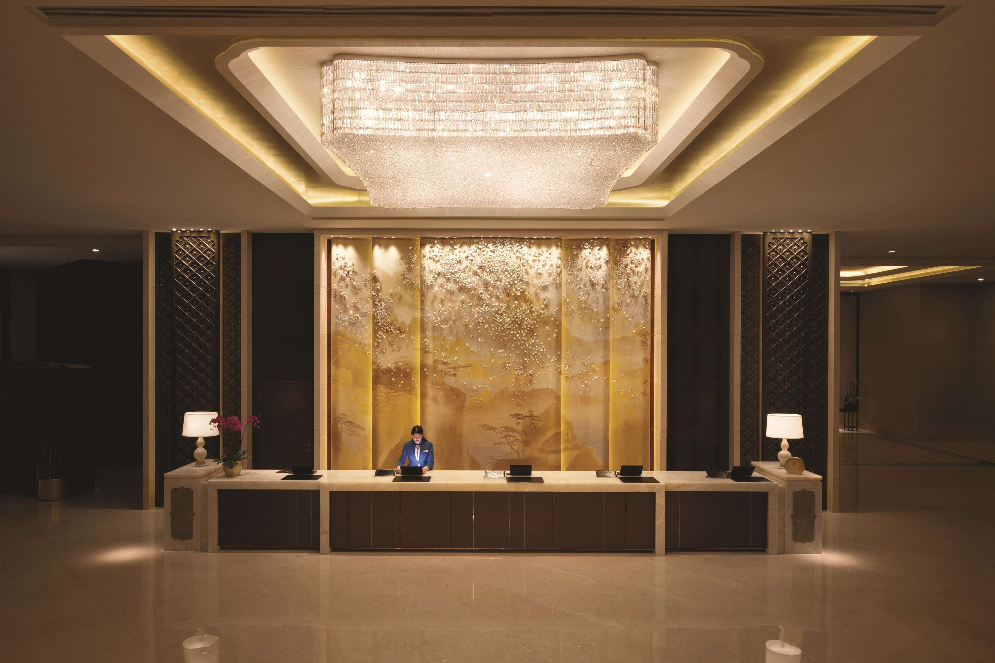 A reception area with a modern chandelier, a receptionist desk, and a decorative wall with a nature-inspired design.