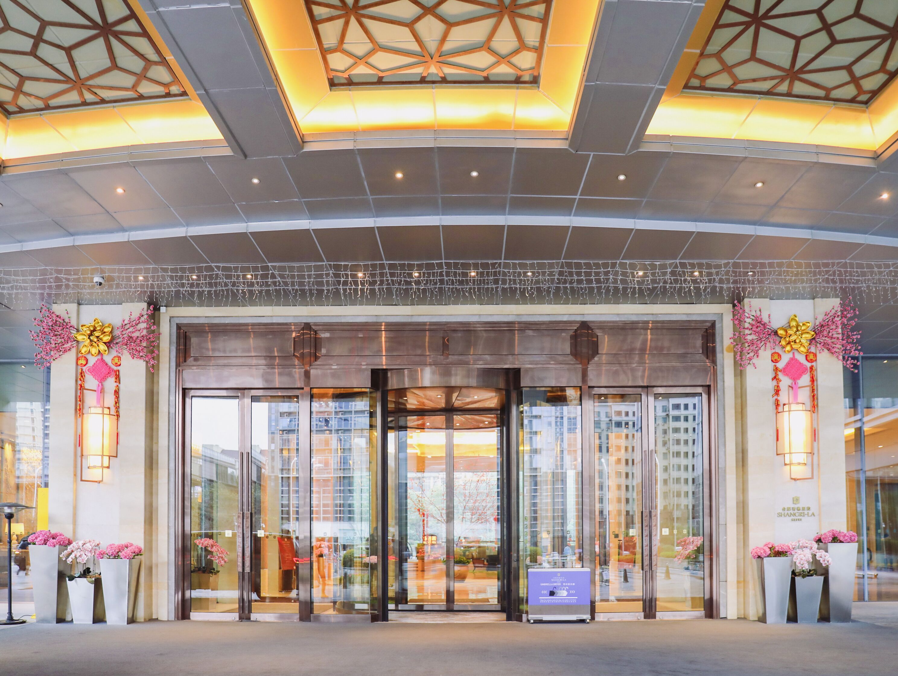 L’entrée d’un hôtel au design moderne, avec une porte d’entrée en verre, un éclairage décoratif et une vue sur le paysage urbain à travers les fenêtres.