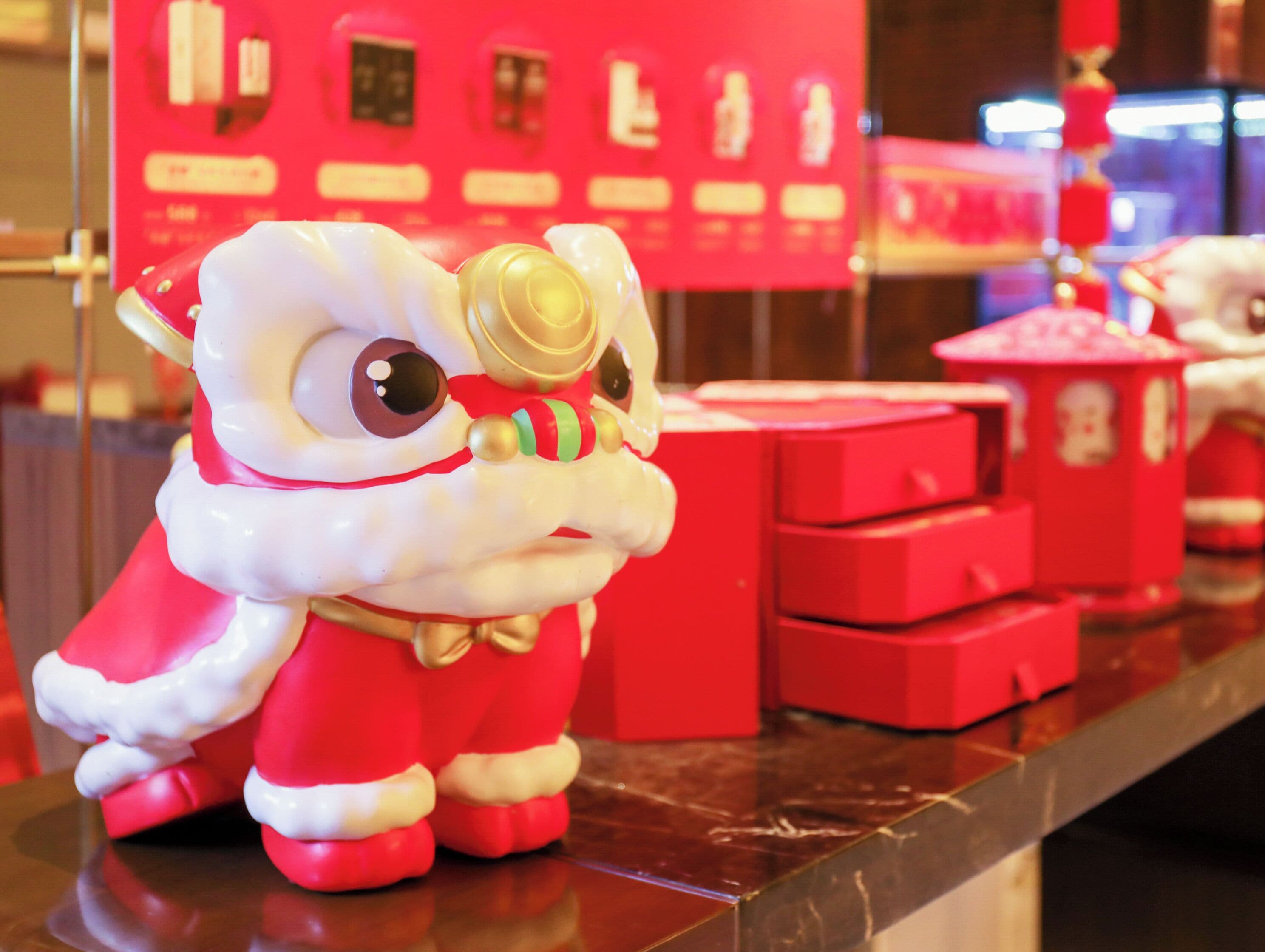 A red and white lion statue on a counter with red boxes in the background.