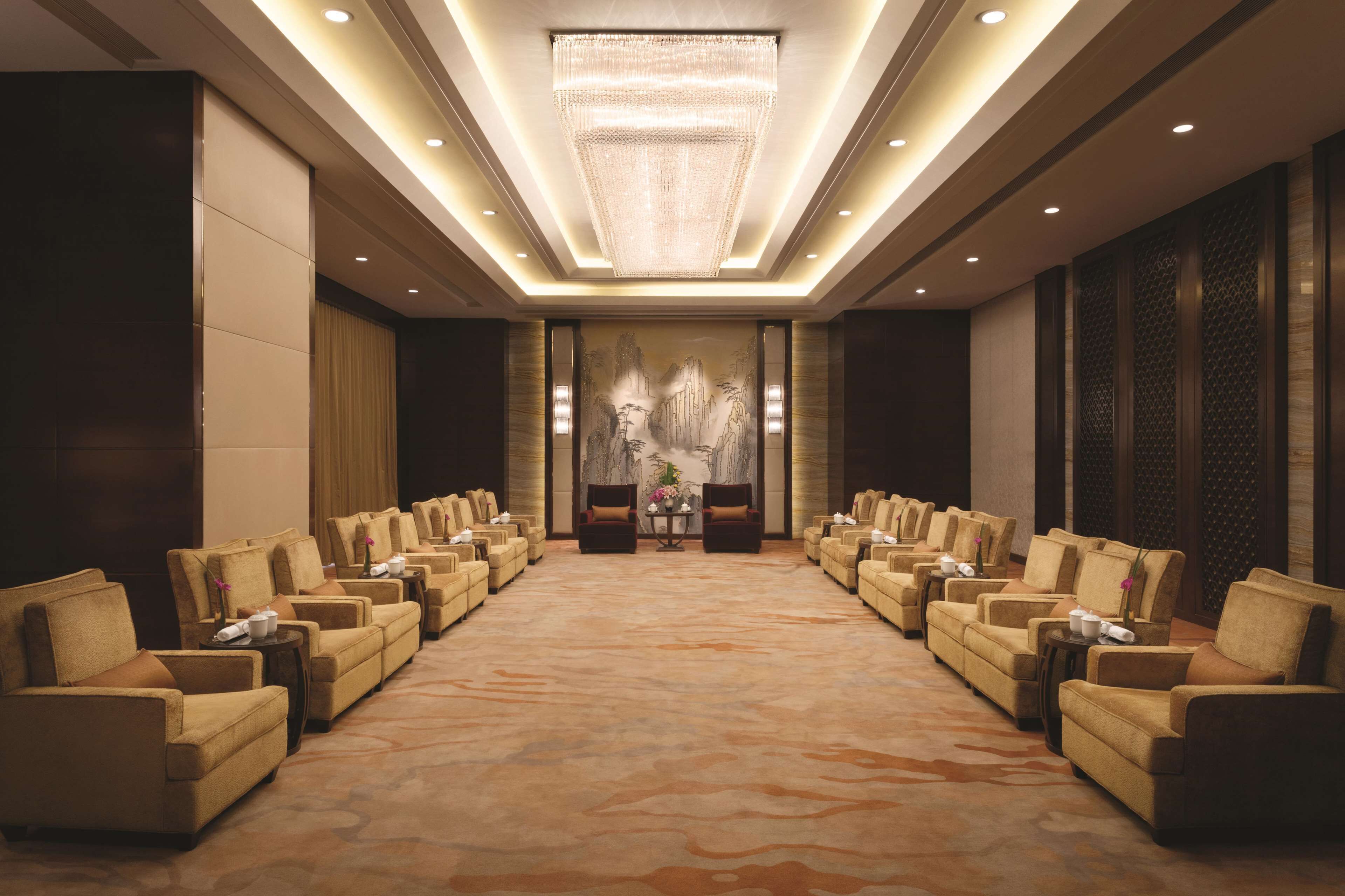 A spacious conference room with rows of chairs, a large chandelier, and a mural on the back wall.