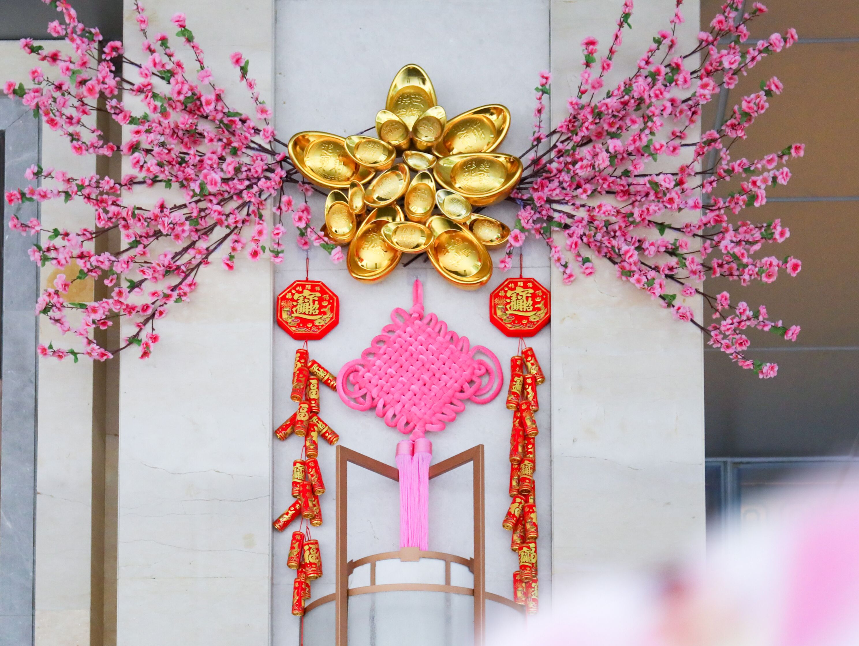 Una decoración con monedas doradas, caracteres chinos rojos y arreglos florales rosados.
