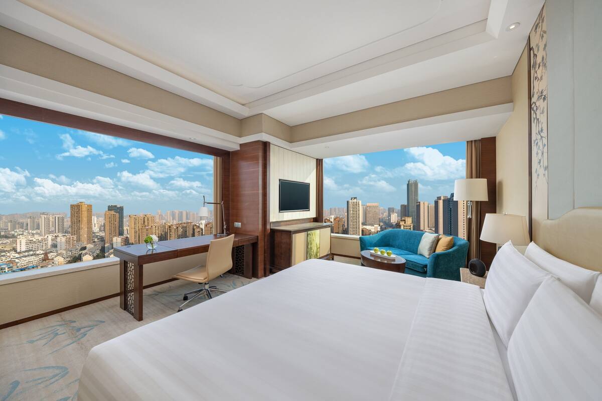 A hotel room with a large bed, a desk, a chair, a sofa, and a TV.