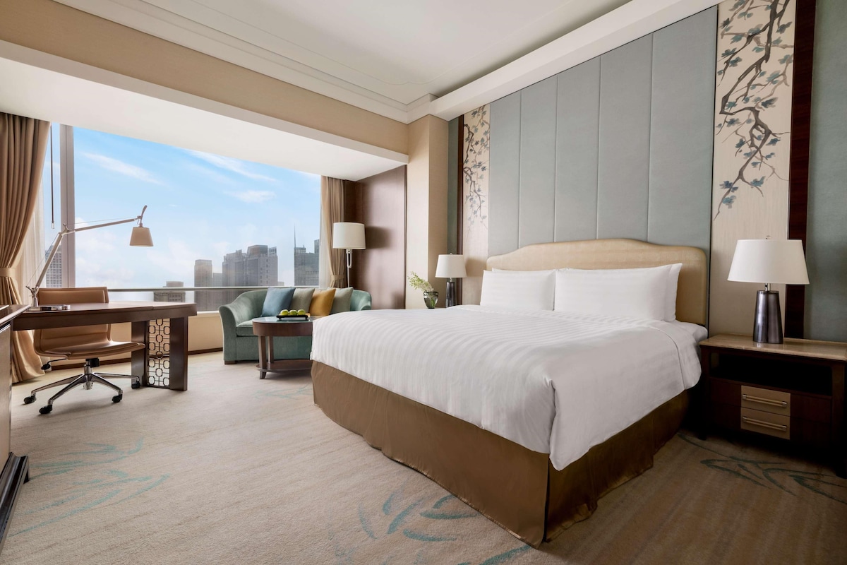 Habitación de hotel con una cama grande, un escritorio, una silla, un sofá y vistas a la ciudad.