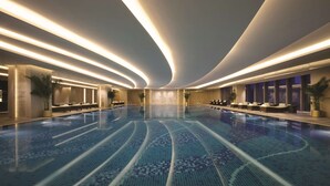 A large indoor swimming pool with a tiled floor and a curved ceiling with integrated lighting. - Shangri-La Hefei (Hefei)