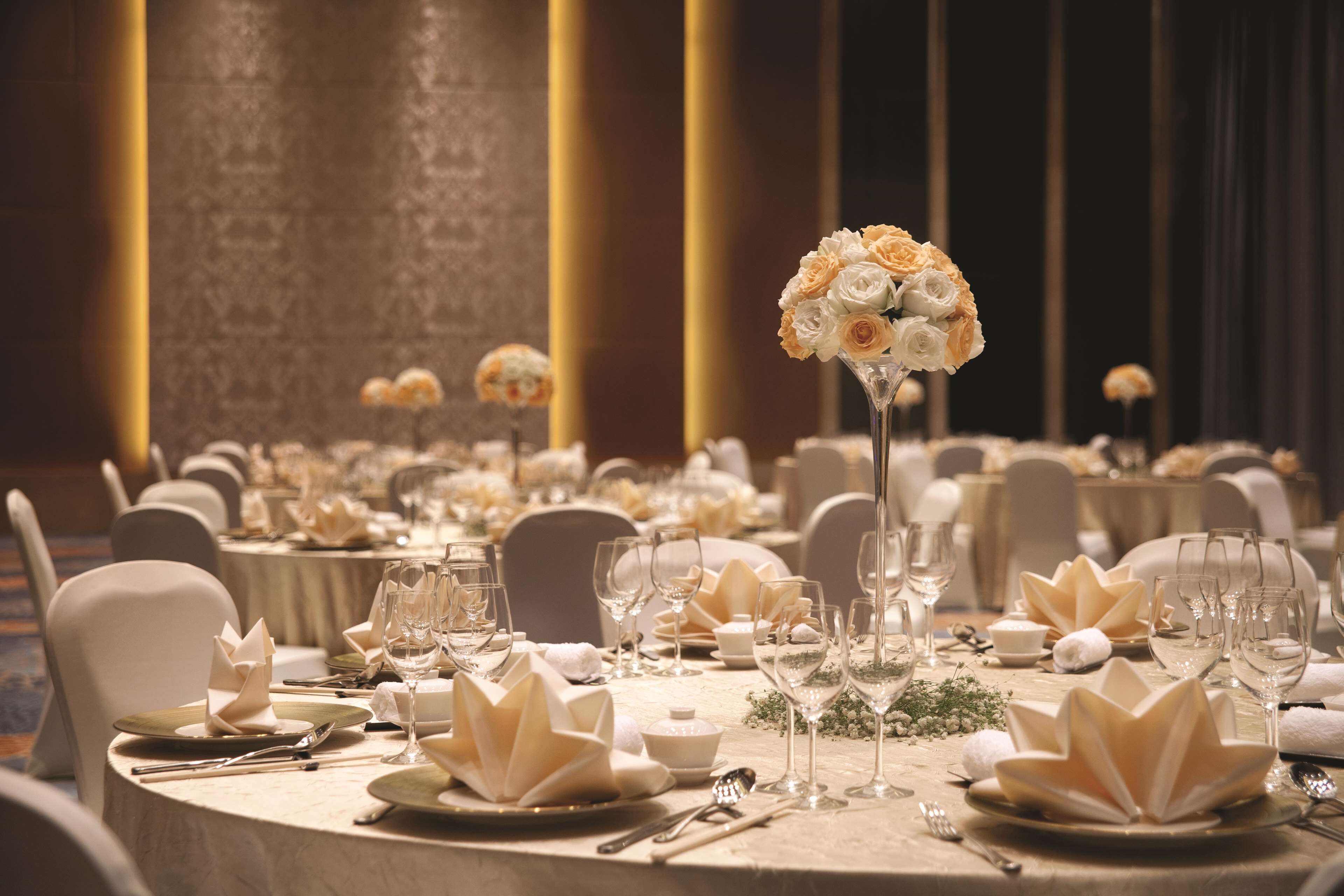 A banquet hall with round tables set for a formal event, featuring floral centerpieces and elegant table settings.
