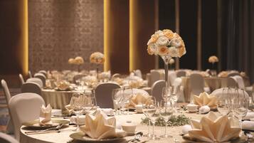 Un salón de banquetes con mesas redondas dispuestas para un evento formal, con centros de mesa florales y una decoración de mesa elegante.