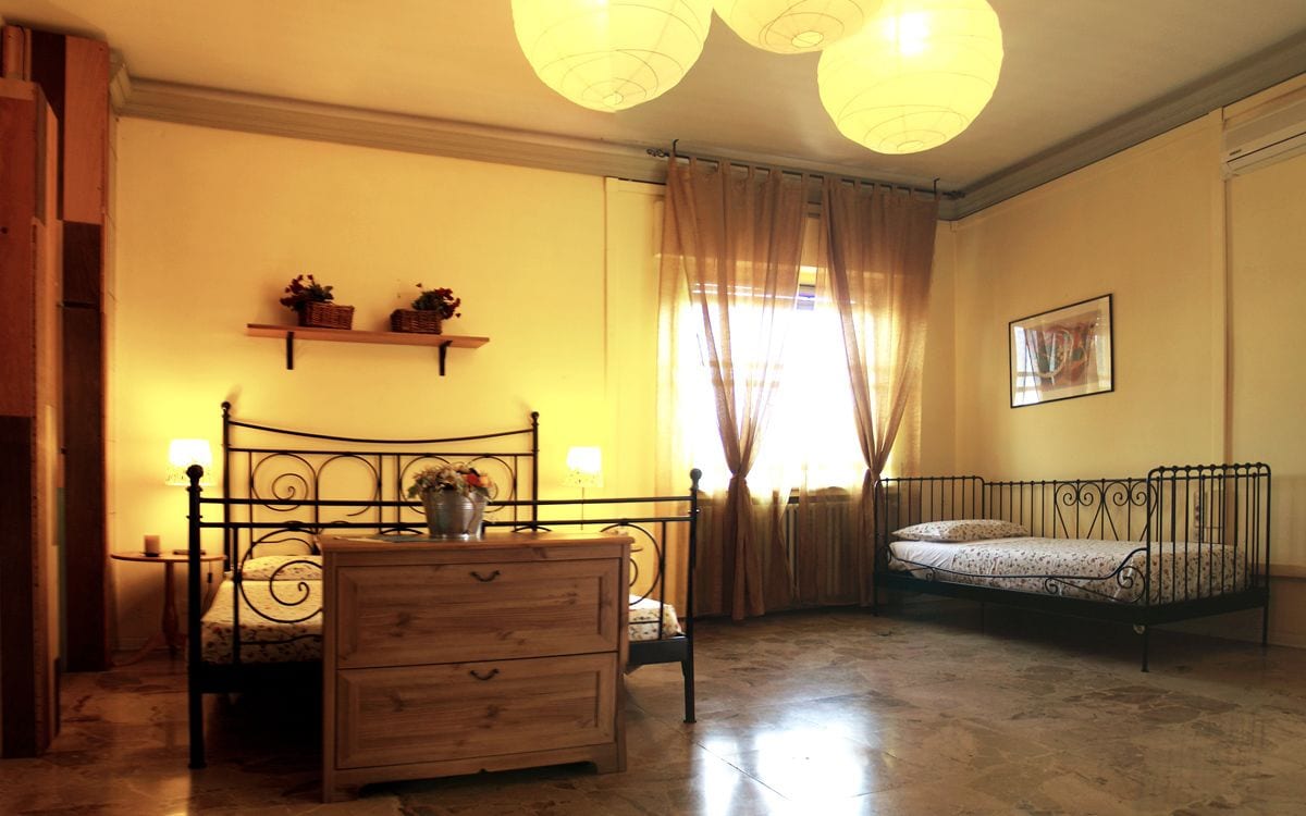 A bedroom with a wooden dresser, a metal bed frame, a small bedside table, and a shelf with plants.