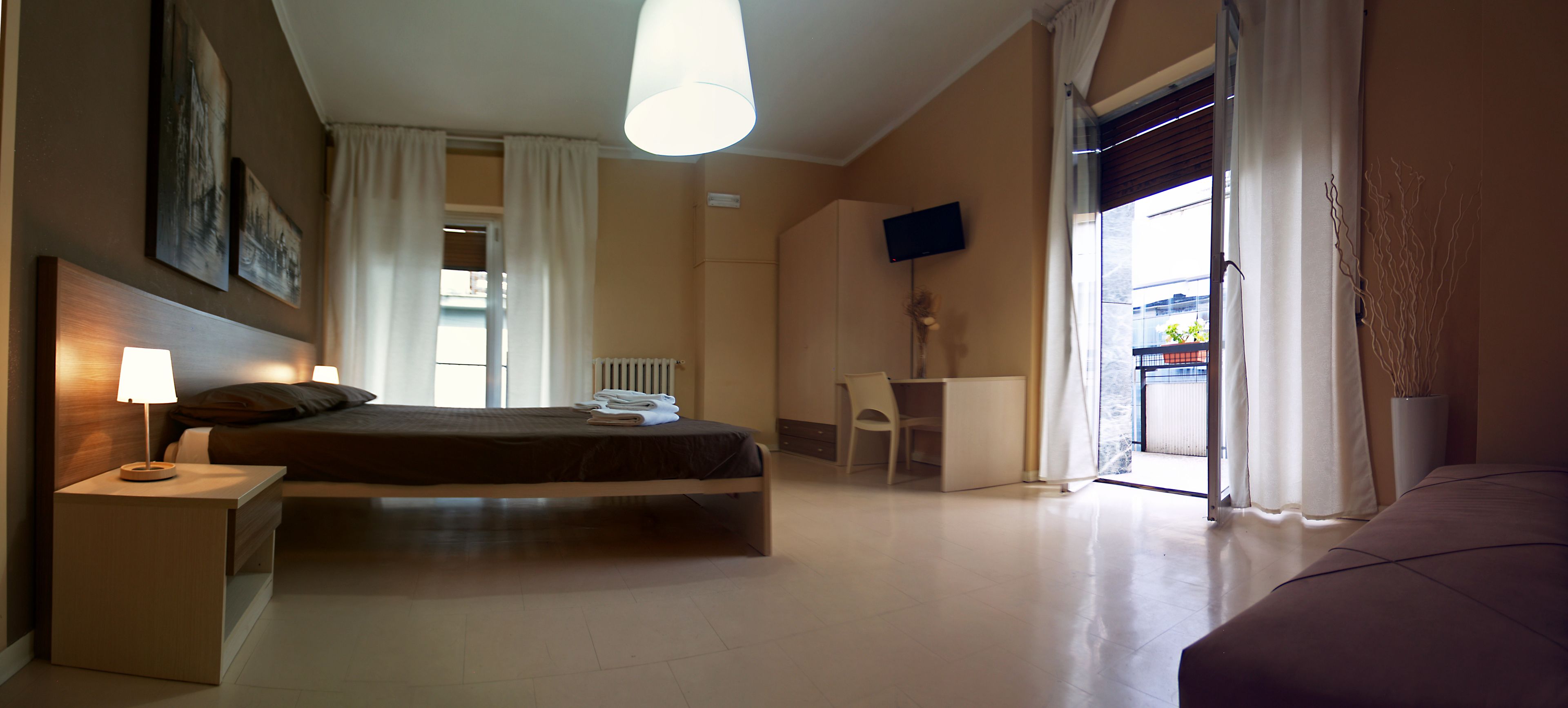 Una camera d'albergo con un letto, comodino, sedia, scrivania, televisore e vista esterna.