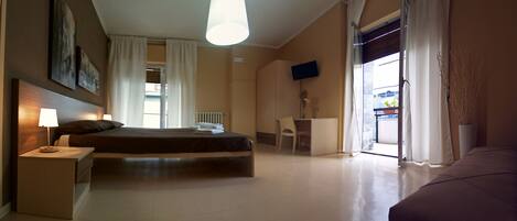 A hotel room with a bed, bedside table, chair, desk, TV, and a view of the outside.