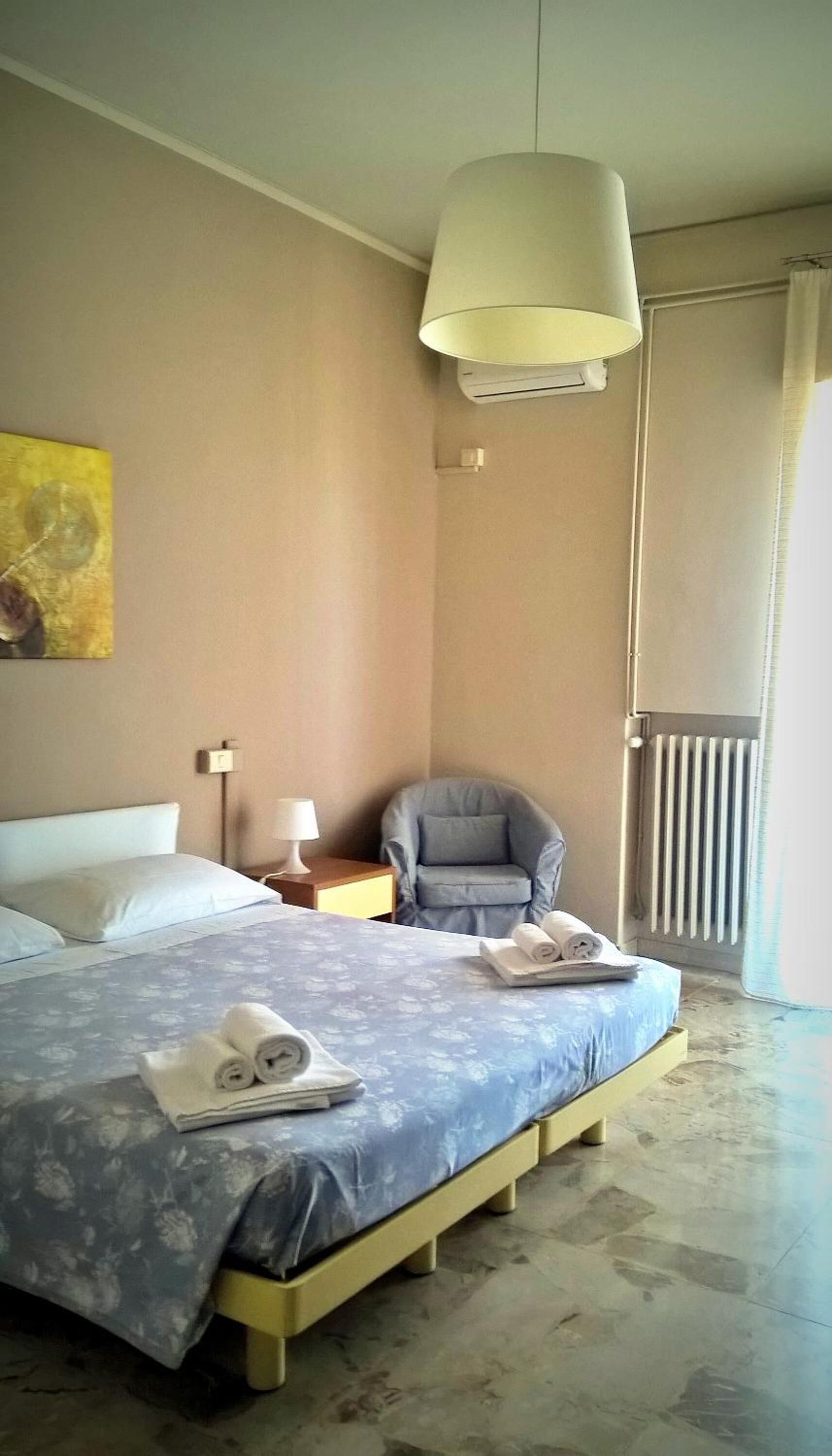 A bedroom with a bed, a chair, a radiator, and a ceiling light.