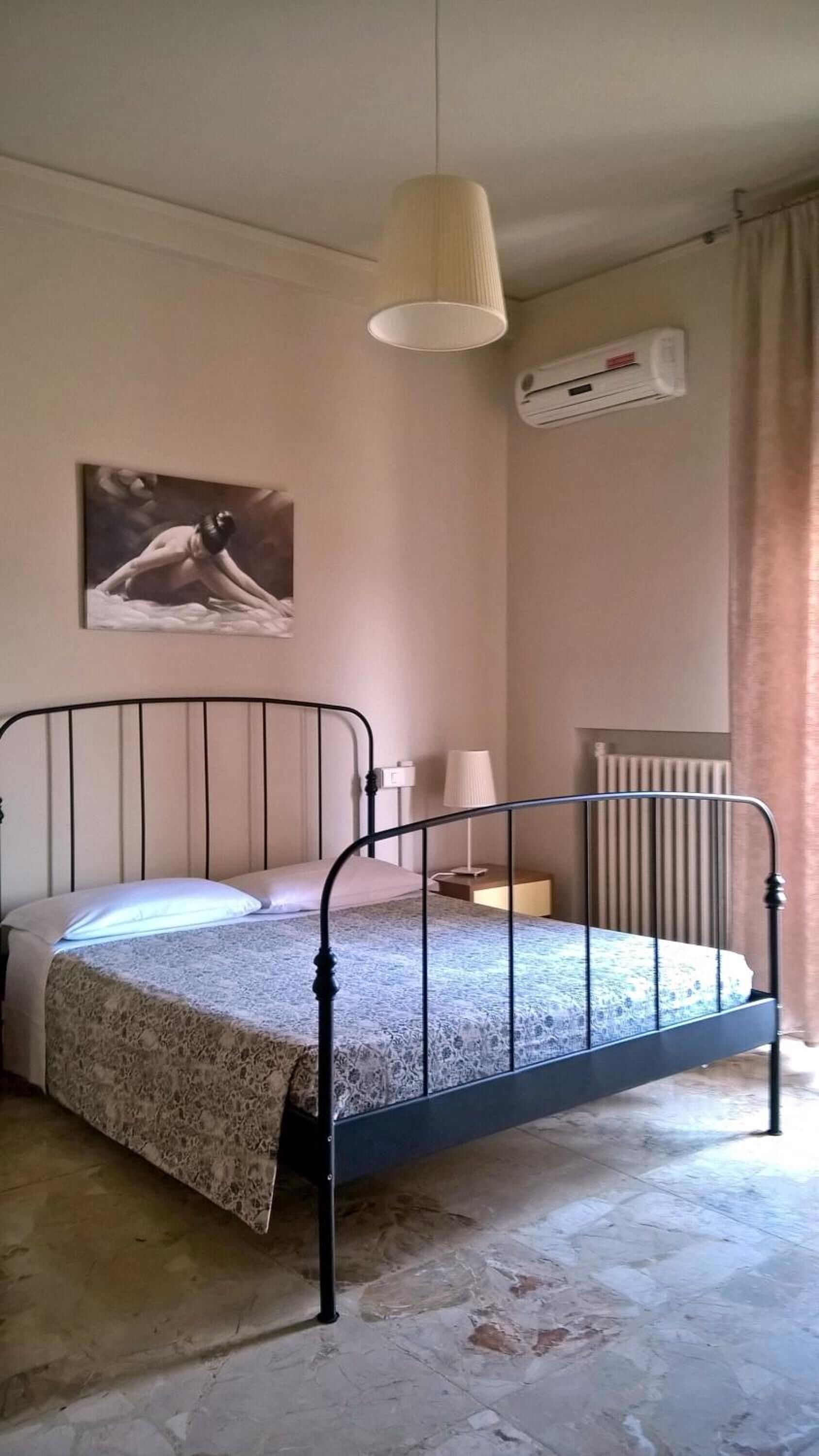Een eenpersoonsbed met metalen frame, een wandairconditioner, een radiator en een schilderij aan de muur.