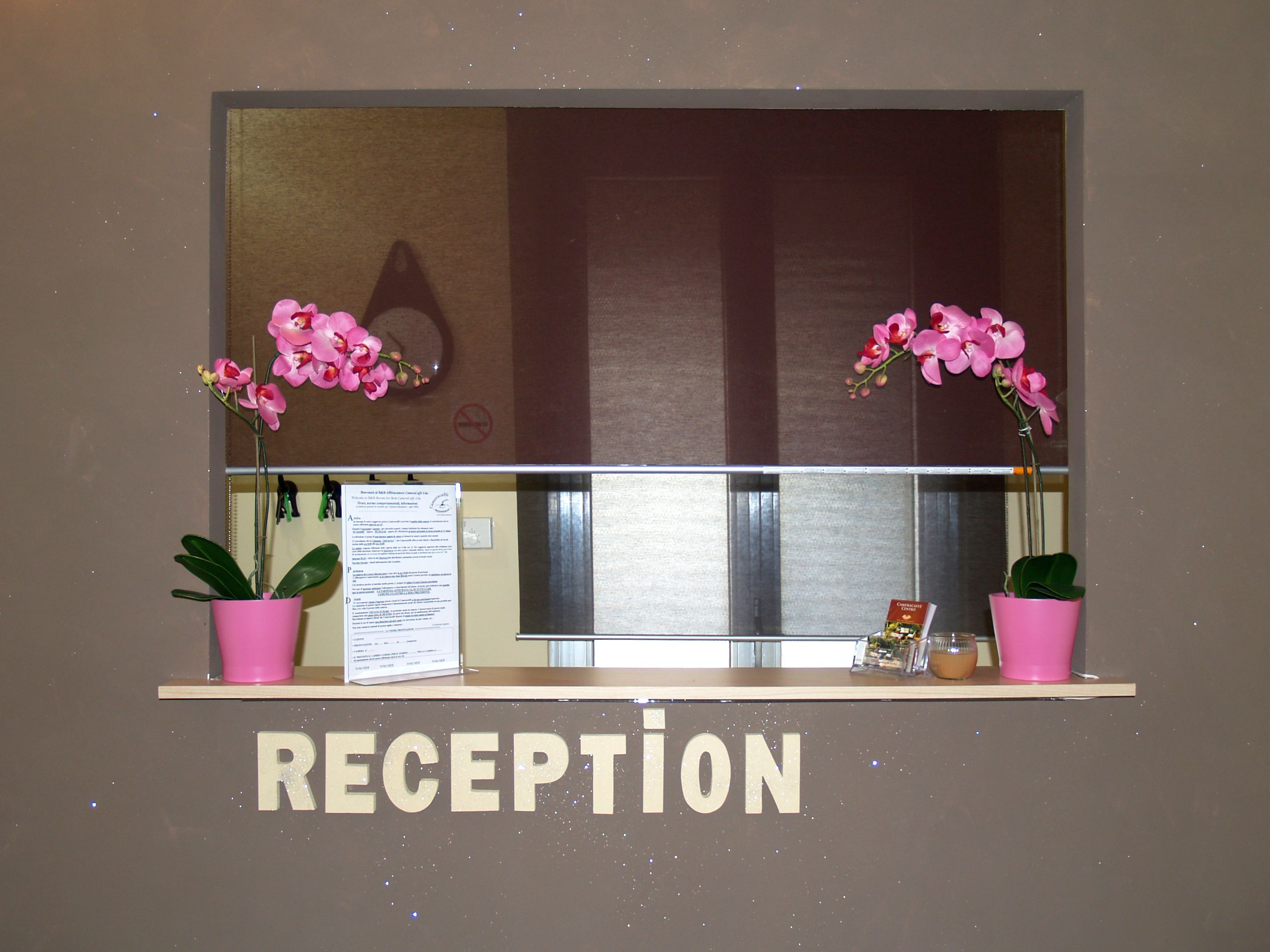 A reception area with a 'RECEPTION' sign, two pink potted orchids, and a menu on the counter.