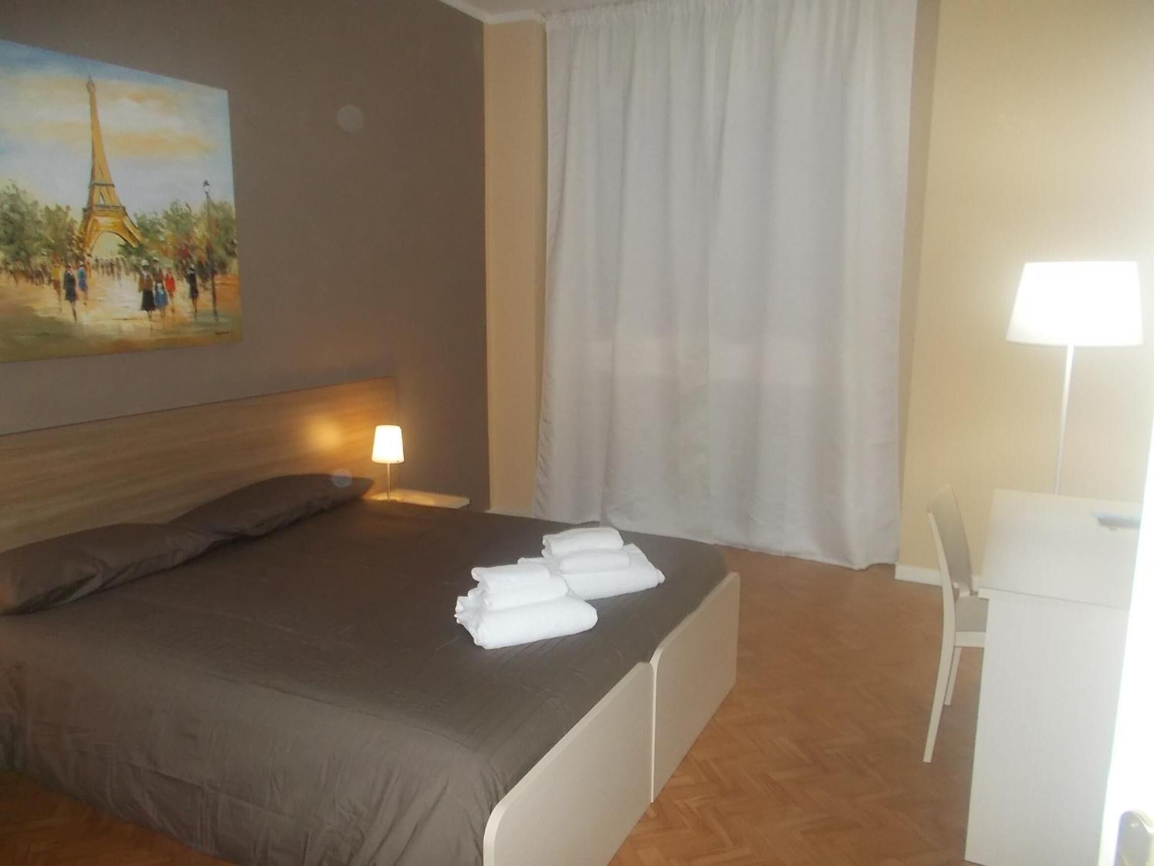 Hotelkamer met een bed, een schilderij van de Eiffeltoren, een nachtkastje met een lamp, een stoel en een bureau.