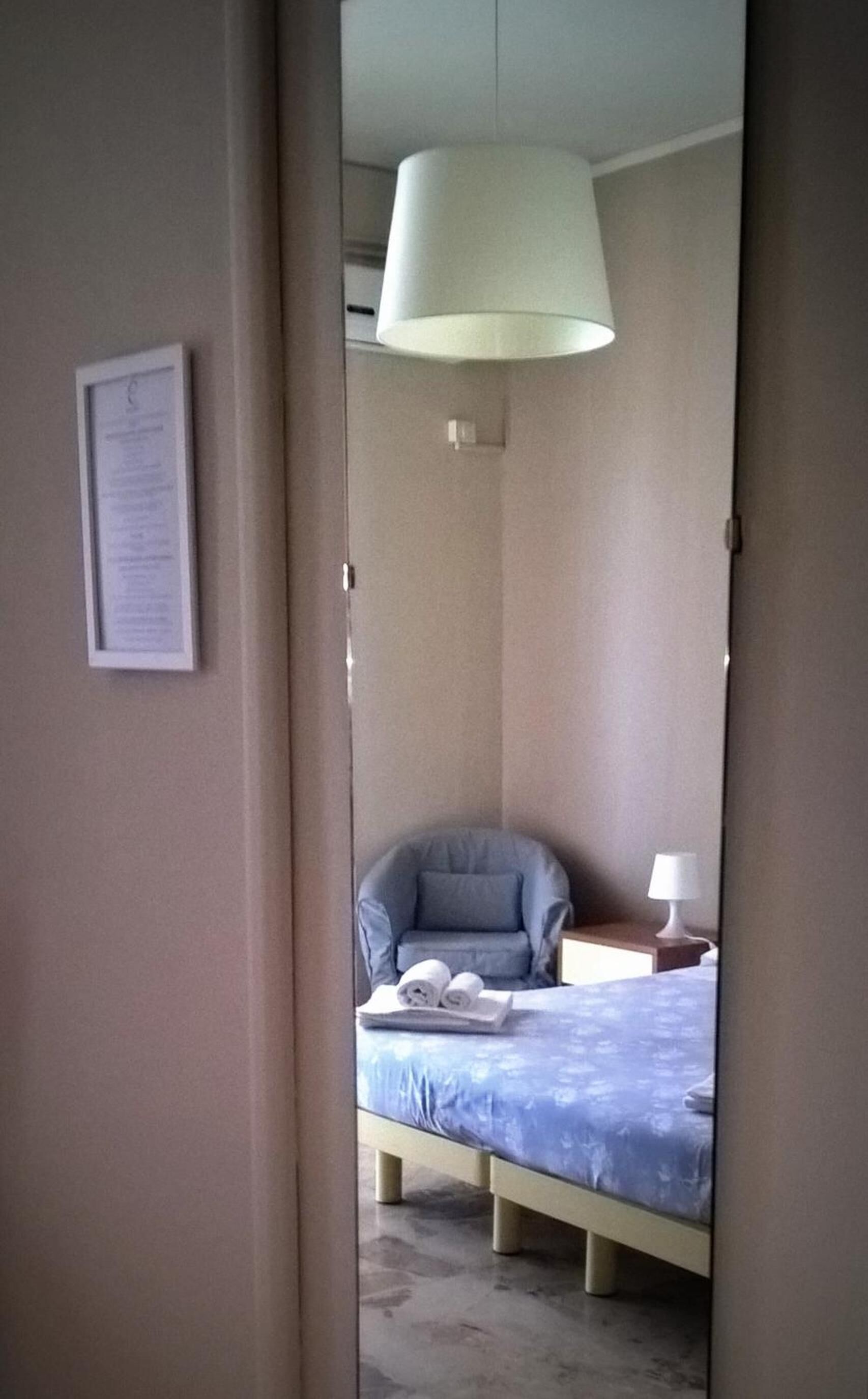 Un dormitorio con cama, una silla, una mesita de noche y una lámpara colgante.