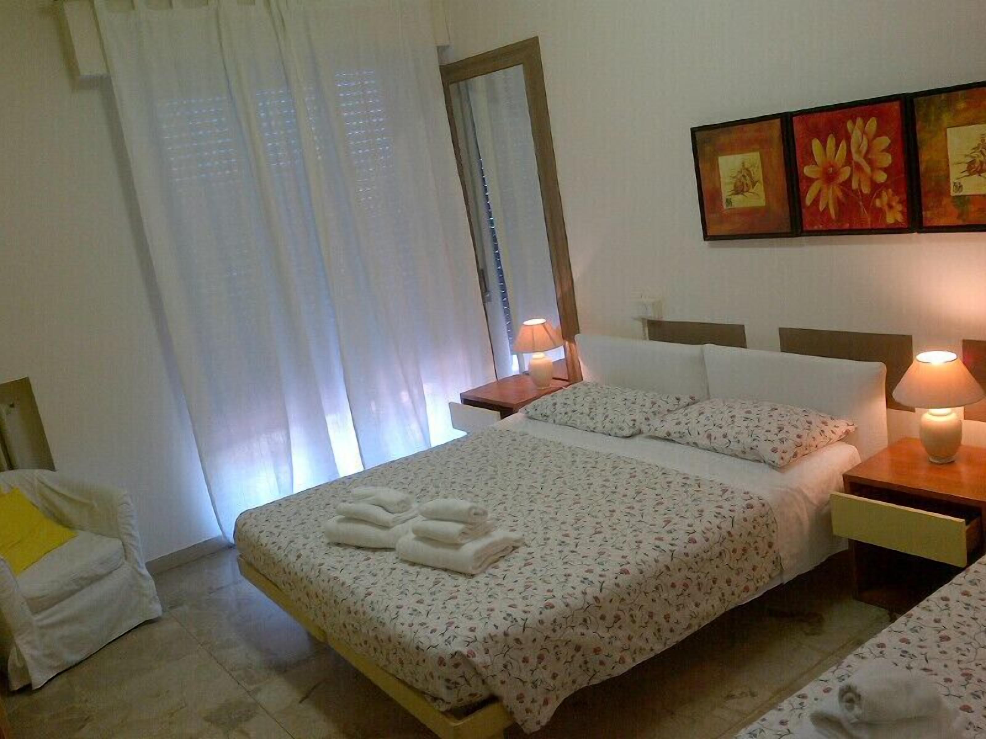A hotel room with a bed, two bedside tables, a chair, and a window with curtains.