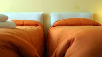 Two beds with orange bedding and white pillows in a room with yellow walls.