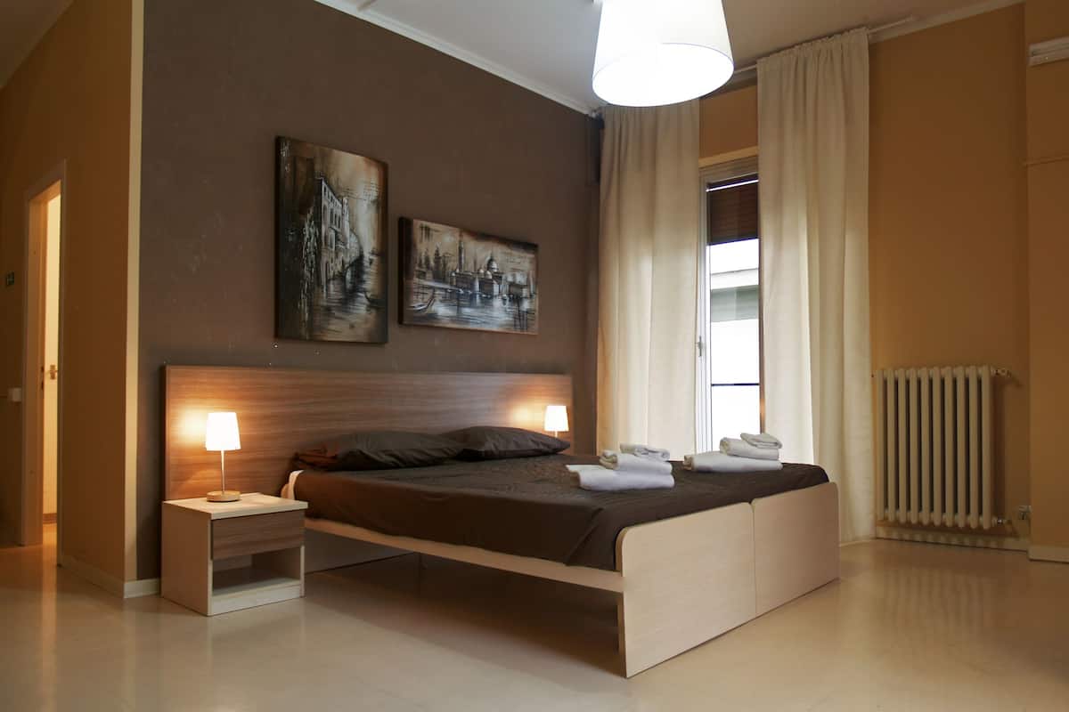 Um quarto moderno com uma cama, mesas de cabeceira, um radiador e obras de arte na parede.