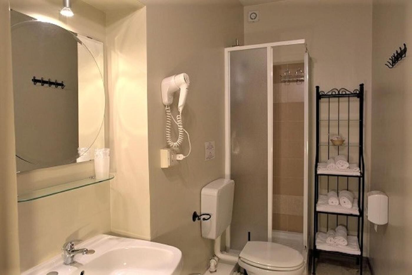 Un baño con cabina de ducha de vidrio, un secador de pelo montado en la pared, un inodoro y un estante con toallas.
