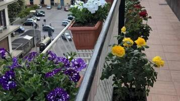 Un balcón con macetas y flores, con vista a una calle con coches y edificios.