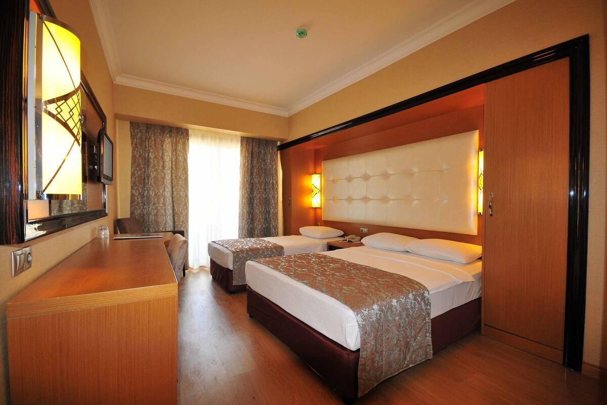 Quarto de hotel com duas camas, uma escrivaninha de madeira, televisão e um espelho grande.