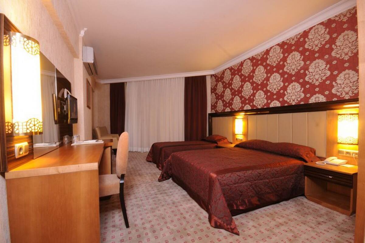 Quarto de hotel com duas camas, uma escrivaninha com cadeira, um espelho e um telefone.