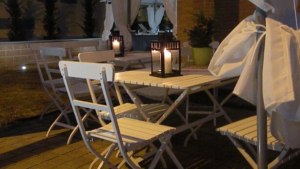 An outdoor seating area with foldable chairs and a table, surrounded by potted plants and a brick wall. - Cameracaffè sul Lago (Arezzo)