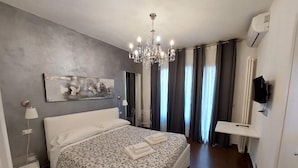 A modern bedroom with a large bed, a chandelier, a flat-screen TV, and a painting on the wall. - Cameracaffè sul Lago (Arezzo)