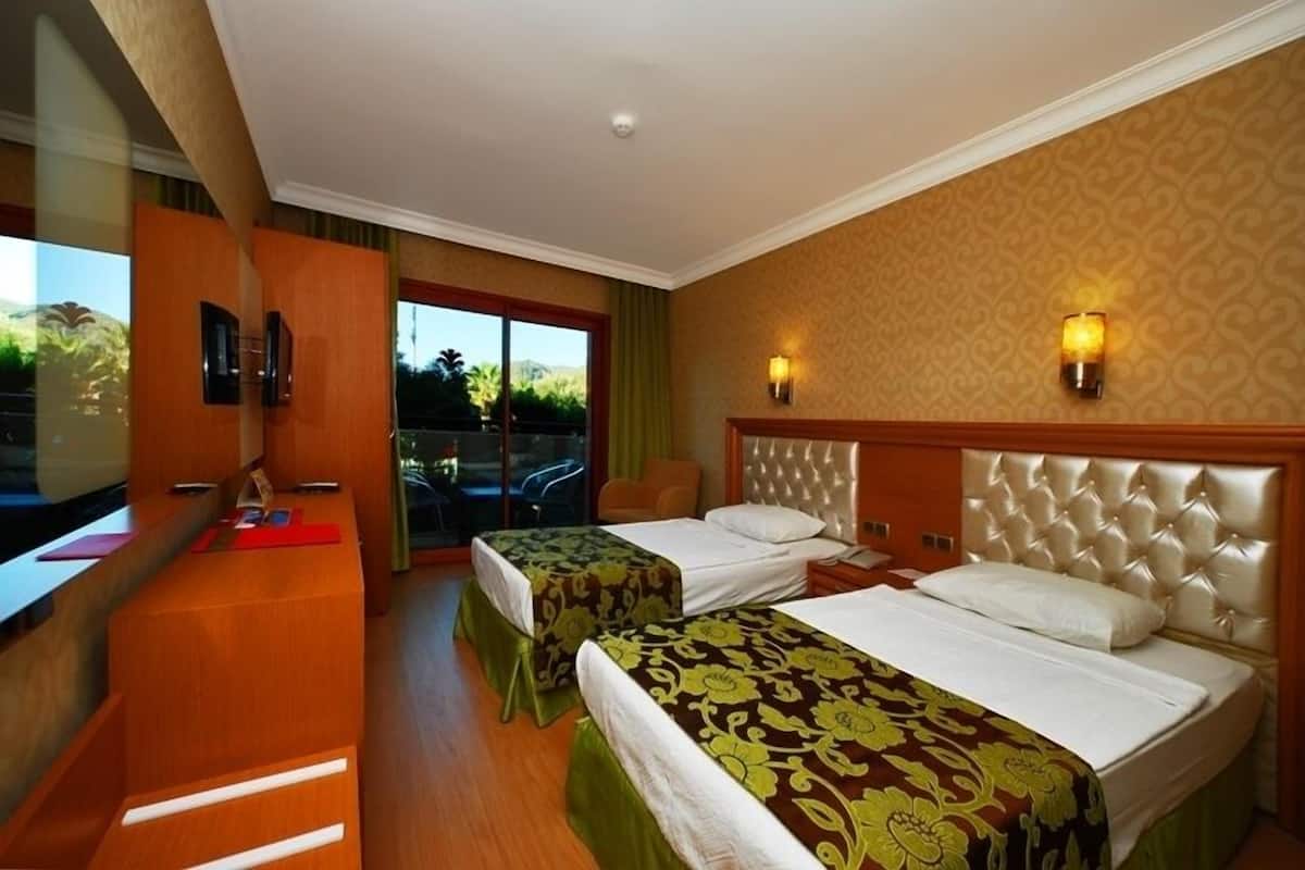 A hotel room with two beds, a wooden desk, and a view of palm trees.