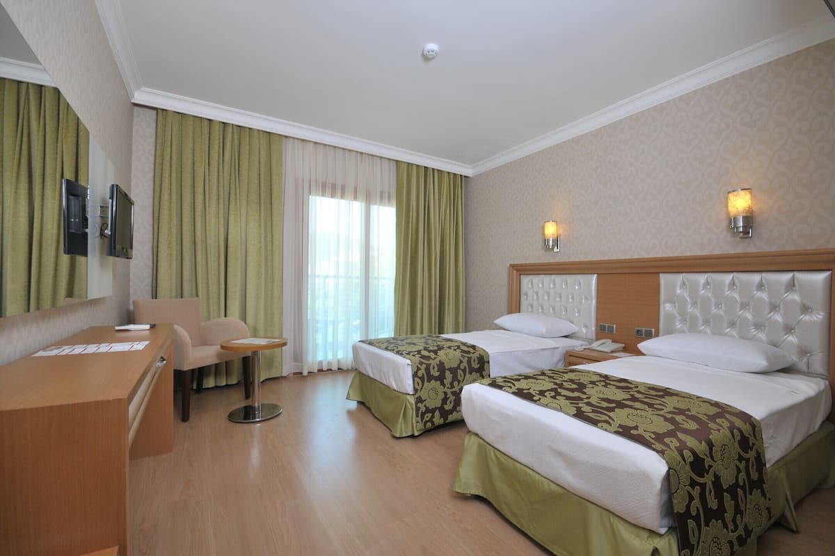 A hotel room with two beds, a desk, a chair, and a small table.