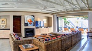 A spacious living area with a large sofa, a fireplace, and a television. - Scallop Guest Lodge (Plettenberg Bay)