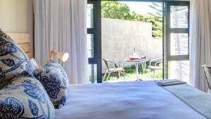 A bedroom with a bed, a nightstand, a lamp, and a view of an outdoor patio with a table and chairs. - Scallop Guest Lodge (Plettenberg Bay)