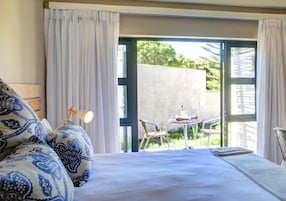 Un dormitorio con cama, mesita de noche, lámpara y vistas a un patio exterior con mesa y sillas.