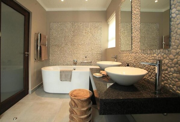 A modern bathroom with a freestanding bathtub, two sinks, and a large mirror.