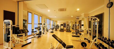 Une salle de sport équipée de divers appareils d’exercice, notamment des machines de musculation et des poids libres, le tout installé sur un plancher en bois.